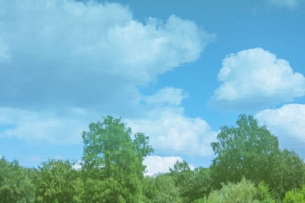 blurred background with clouds, blue sky and green trees