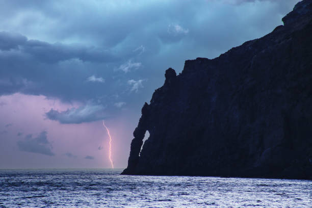 Lightning strikes over the stormy sea horizon of Pantelleria island, illuminating rugged cliffs, dark clouds, and turbulent Mediterranean coastal waters.