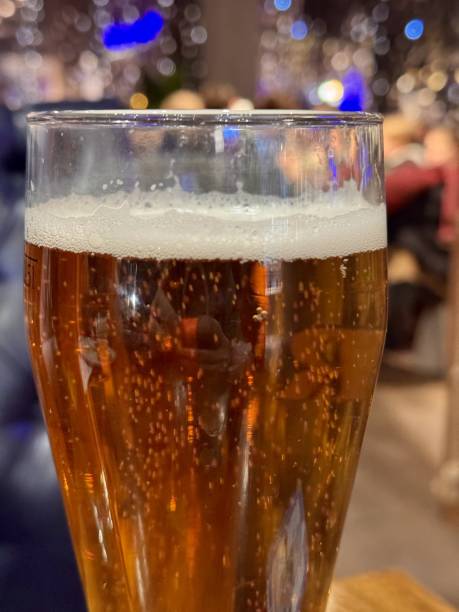 istock One tall glass filled with refreshing golden lager beer, bubbling delightfully on a rustic wooden surface. Refreshing Cold Beer Served in Pint Glasses Resting on a Rustic Wooden Table Surface 2203289392