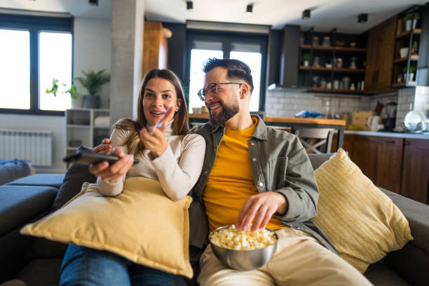 istock Young couple watching tv and having popcorn on sofa at home 2203291074