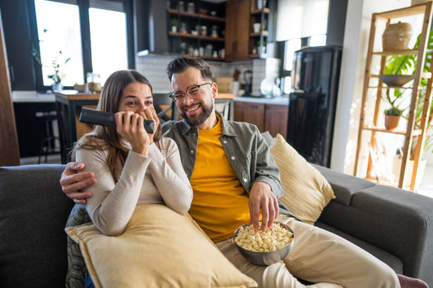 istock Couple watching tv and eating popcorn on sofa at home 2203291124