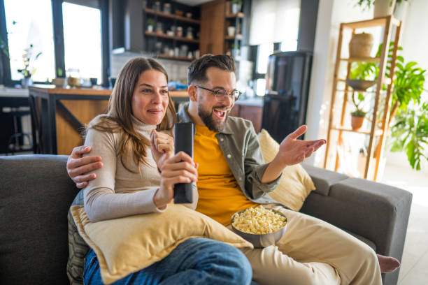 istock Excited couple watching tv and eating popcorn on sofa 2203291131