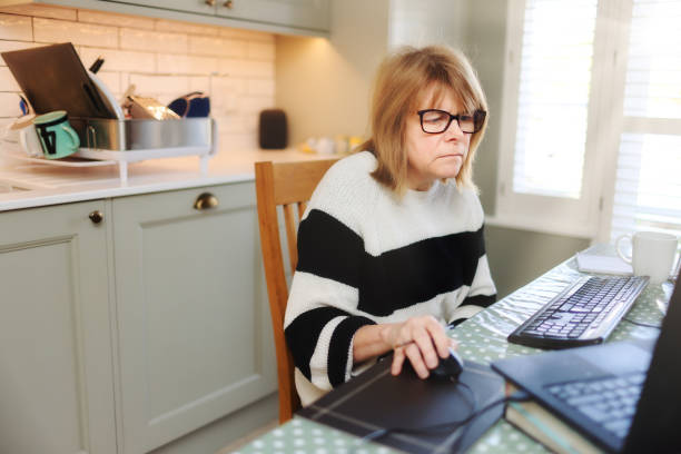 istock Middle aged woman home-working from her kitchen at a computer screen 2203293710