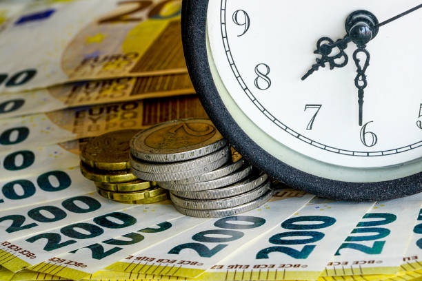 istock Fragment of an analog table clock face on a stack of euro banknotes, business concept. Time is money 2203294030