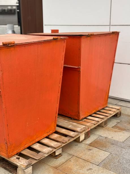 istock Orange Waste Bin Positioned in an Urban Setting, Complete with Black Stands for Support. In modern urban environment, an orange waste bin is strategically placed on pallet, surrounded by sleek metal 2203294117