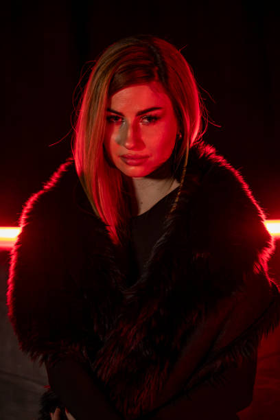 A lady poses in a black fur coat and hugs herself.