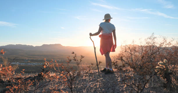 Mature woman stands on top of hill in desert landscape at sunset, looks out, Tonto Basin, AZ