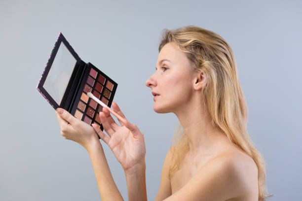 istock Woman with Long Blonde Hair Applying Makeup Using a Gorgeous Eyeshadow Palette for a Glamorous Look and Beauty Enhancement in a Casual Setting 2203306425