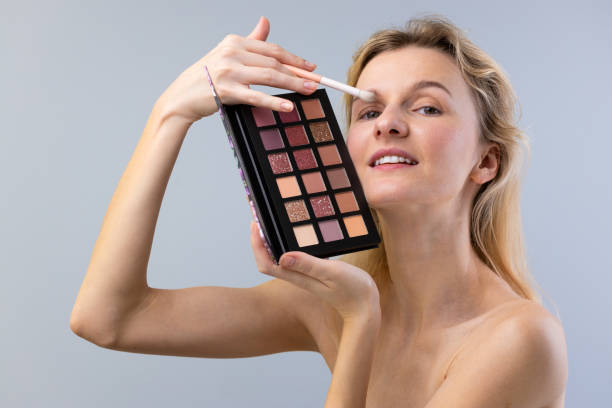 istock Beauty Enthusiast Showcases a Colorful Eyeshadow Palette While Applying Makeup With a Brush to Enhance Her Eye Look for a Glamorous Appearance 2203306826