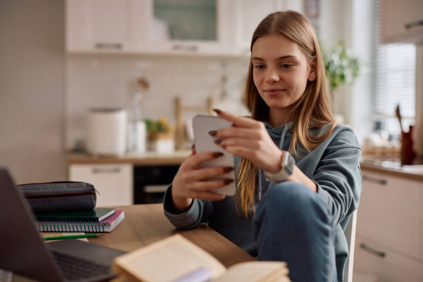 istock Smiling teenage girl using app on smart phone while studying at home. 2203312553
