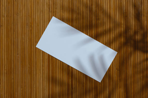 istock Blank white paper leaflet template displayed on textured bamboo wood surface with natural palm shadows. 2203314935