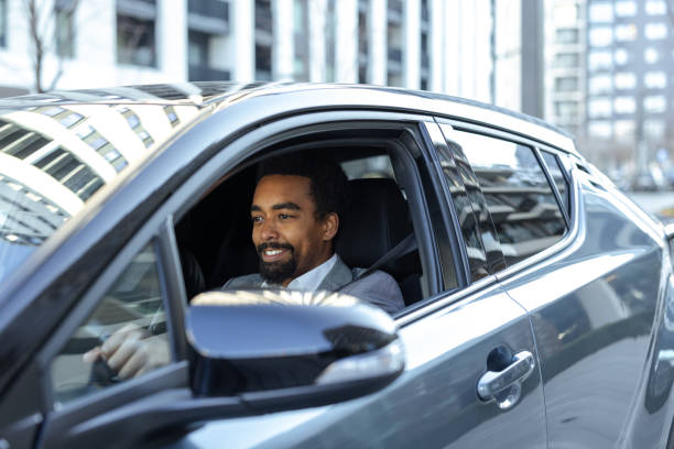 istock Smiling man driving a car on a bright day in a modern city 2203320167