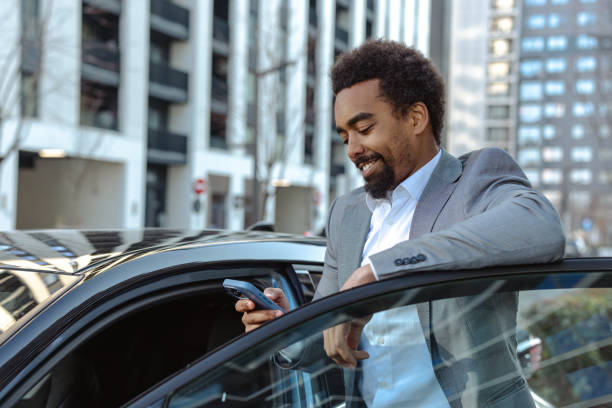 istock Smiling businessman leaning on a car in an urban setting and using smartphone 2203320874