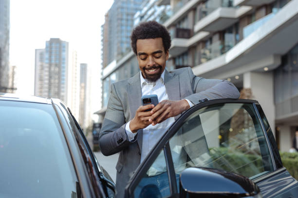 istock Smiling businessman leaning on a car in an urban setting and using smartphone 2203320876