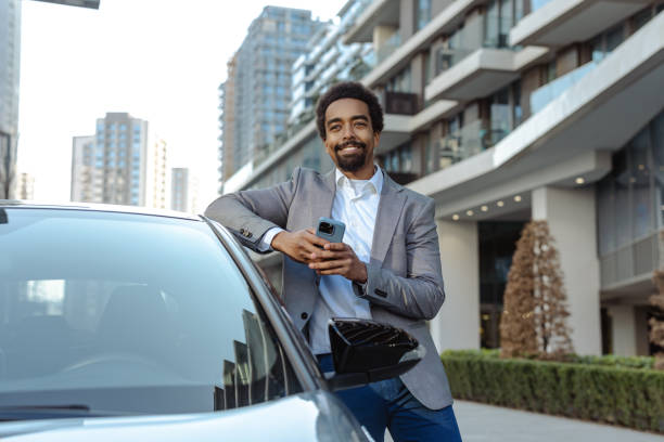 istock Smiling businessman leaning on a car in an urban setting 2203320877