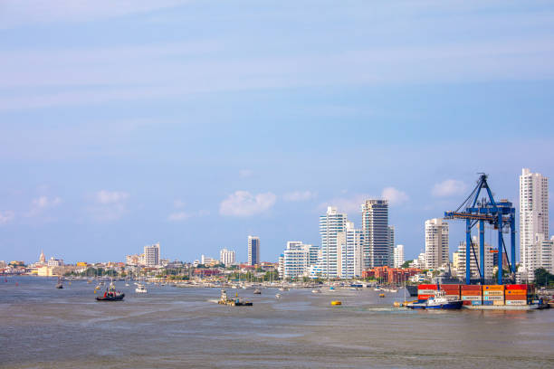 This photo captures a stunning aerial view of Cartagena de Indias, a historic port city on Colombia's Caribbean coast. From this vantage point, we can observe the city's unique geography, with the clear turquoise waters surrounding a peninsula densely packed with modern high-rises that define the city's skyline. The contrast between the blue of the sea and the urban architecture is striking, with the city appearing as a bustling metropolis rising from the coastal landscape. The sky above is a serene blue, hinting at favorable weather. Small boats can be seen in the water, emphasizing the city's connection to the sea. This perspective provides a comprehensive glimpse of Cartagena's blend of natural beauty and urban development.