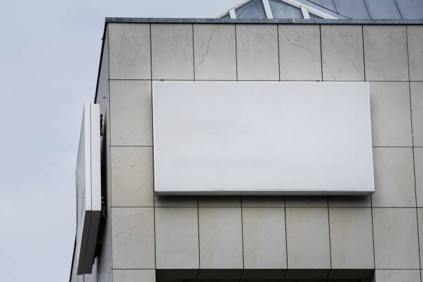 An empty rectangular white sign attached to the exterior wall of an office building in Germany. The simple design and neutral color offer ample room for promotional or informational displays, making it a versatile and highly visible advertising space. The modern building facade provides an urban context, highlighting the potential for corporate branding or local business announcements in a bustling metropolitan environment. usage only,