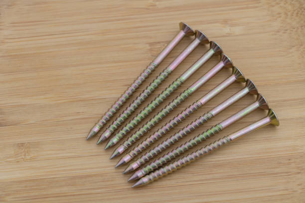 6 Phillips-point head carpenter nails laying on a light wood surface, with yellow-green colored nail heads.