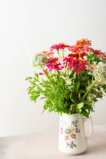 Summer bouquet of colorful Zinnia, onion inflorescences and mint sprigs, bouquet of flowers on the table near the wall, home decoration with flowers