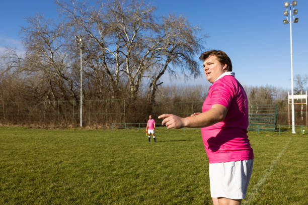 Referee in pink jersey officiating a football match on a sunny day in a park