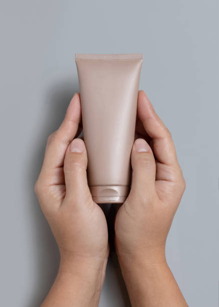 istock Hands holding light brown squeeze cream tube over grey top view, cosmetic mockup, copy space 2203335526