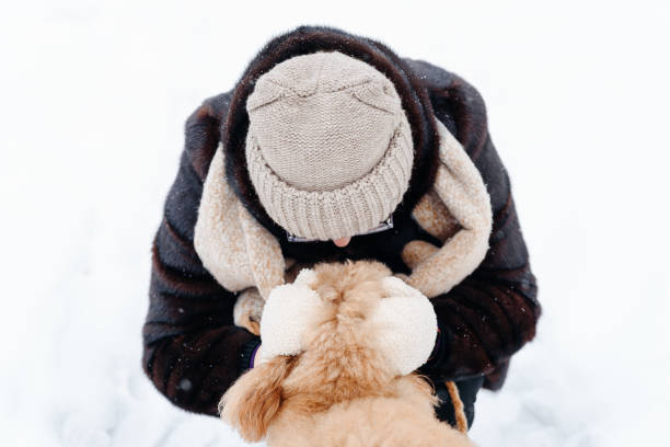young woman hugging her dog, red poodle standing on white snow in winter day, dogwalking concept, unrecognizable