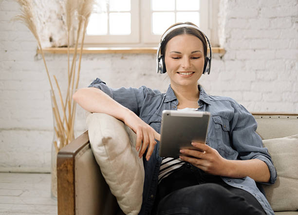 istock Beautiful young woman using digital tablet, watching movie while relaxing on her sofa in living room. 2203336168