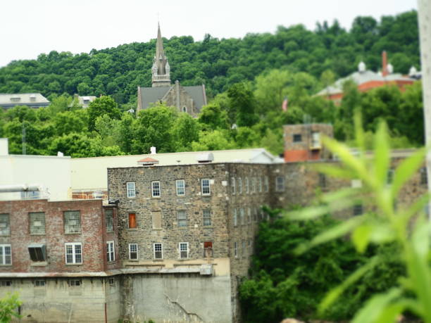 Stone and brick building along a river with green trees and a church in the distance