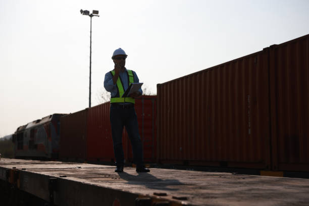 istock Middle Eastern male engineer railway worker wearing a hard hat and safety vest checking the container cargo and working with a walkie-talkie at the station near freight trains. 2203344920