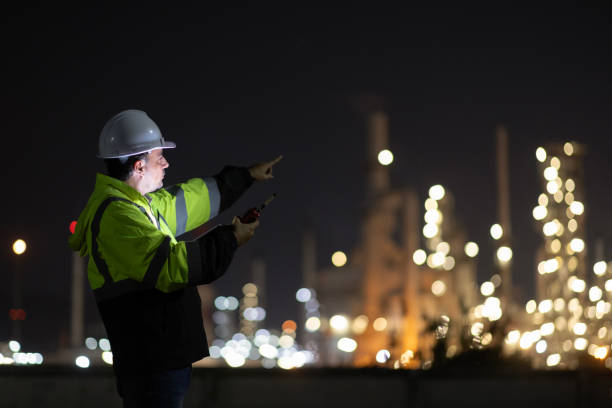 istock Male Middle Eastern engineer wearing a bright green safety jacket, including hard hat examining the survey are using tablet and walkie- talkie to collaborate and discuss screen work plant site use with night lights of oil refinery industry background. 2203349926