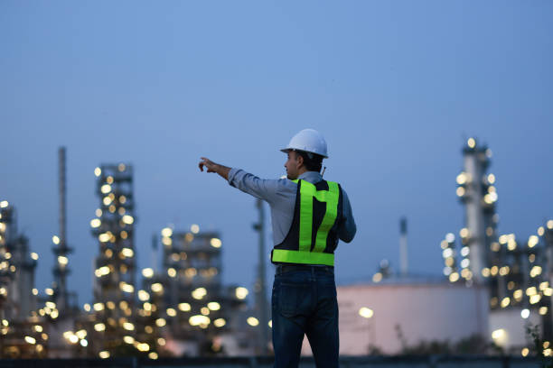 istock Male Middle Eastern engineer wearing a bright green safety jacket, including hard hat examining the survey are using tablet and walkie- talkie to collaborate and discuss screen work plant site use with night lights of oil refinery industry background. 2203352898