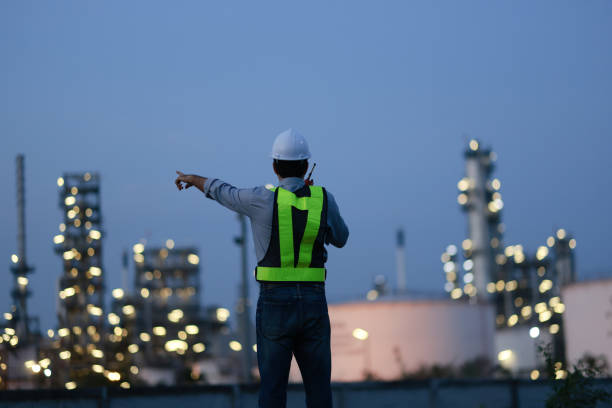 istock Male Middle Eastern engineer wearing a bright green safety jacket, including hard hat examining the survey are using tablet and walkie- talkie to collaborate and discuss screen work plant site use with night lights of oil refinery industry background. 2203352905