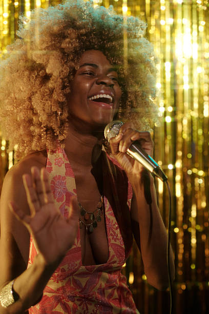 istock Performing Singer in a Sparkly Gold Backdrop Holding Microphone 2203358531