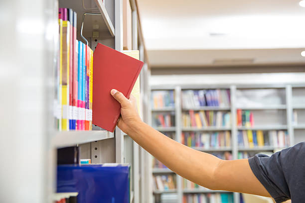 istock Close up hand picking a book from bookshelf in the library. Concepts for reading textbook and school for student knowledge education. 2203360708