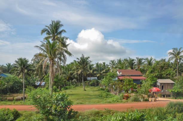 Phnom Penh, Cambodia - May 6, 2009: Peaceful village with palm trees and red dirt road under bright midday sun.