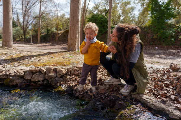 istock Mother and son holding hands and looking at stream in forest 2203364827