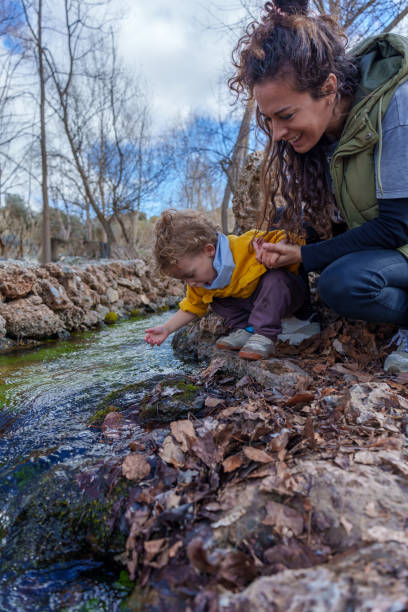 istock Mother and child exploring nature and touching water in a stream 2203364856