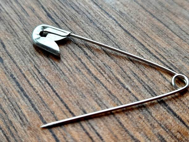 istock One open metal safety pin with wooden background. 2203365193