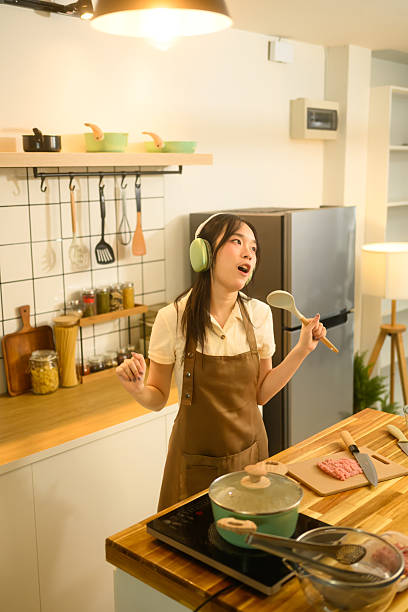 istock Cheerful woman wearing head phone singing while cooking in a stylish kitchen 2203365393