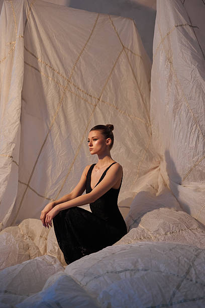 istock model sits gracefully on soft, textured fabric in a black dress, surrounded by draped materials in a warm and inviting studio environment, evoking calm and elegance during a fashion shoot 2203365574