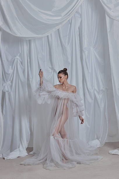istock model stands poised in an airy setting, dressed in delicate sheer fabric that flows elegantly around her. soft drapery adds a dreamlike quality to the artistic display of fashion 2203365583