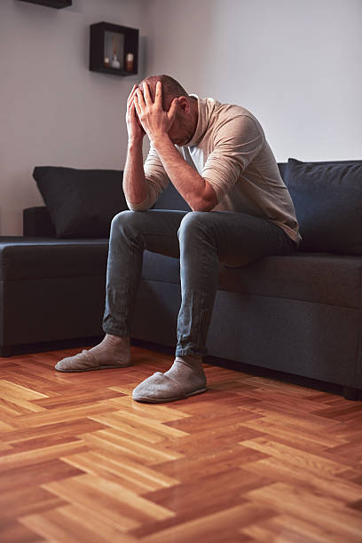 istock Man with headache and depression sitting on a sofa at home. 2203366018