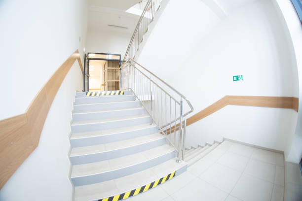 A wide-angle view of a bright and modern staircase in a commercial building, featuring stainless steel railings and tiled steps. Represents architecture and safety.