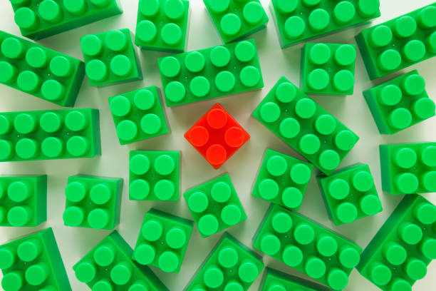 Green plastic blocks around red block on white table background. Concept of individuality. Closeup. Top down view.