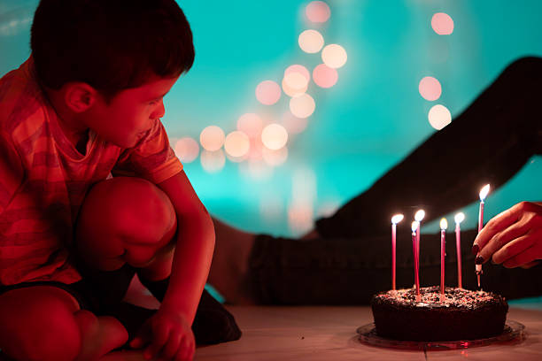 Child watching parent lighting candles on birthday cake with beautiful bokeh effect