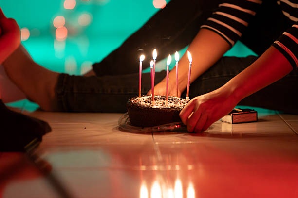 Group of friends celebrating birthday at home and lighting candles on birthday cake
