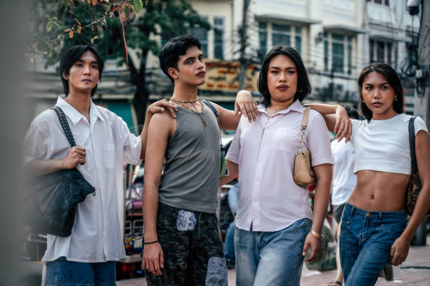 Diverse group of LGBTQ friends , casually dressed and standing together on street, arms on shoulders, looking at each other and camera