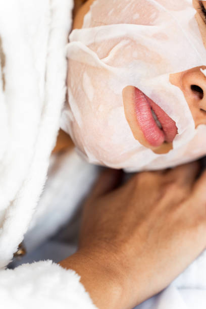 Close-up of a young woman wearing a moisturizing face mask while relaxing in her bathrobe, enjoying a moment of skincare and self-care