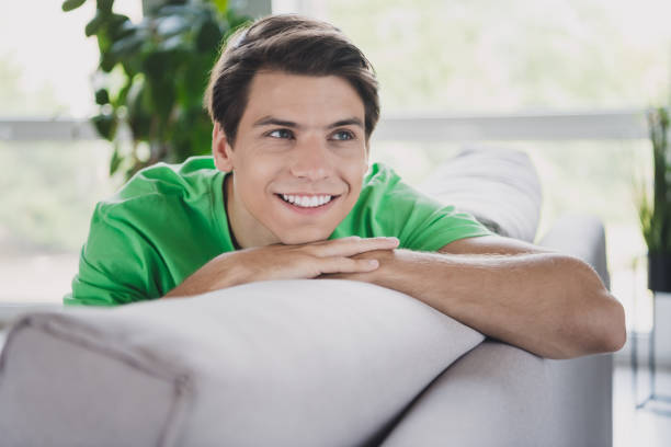 istock Young man relaxing indoors on a sofa, smiling cheerfully in a bright and cozy home interior surrounded by natural daylight 2203375421