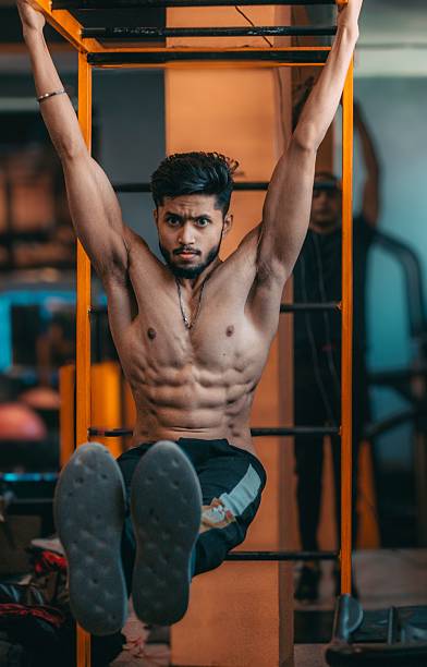 A young man in a gym performing a hanging leg raise exercise, showcasing muscular physique and strength training.